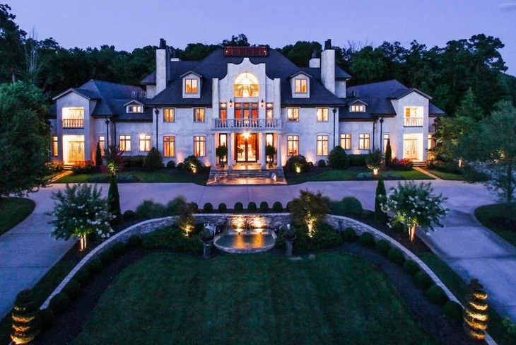 Exterior view of Bill Wyman's house, a historic building with elegant architecture, surrounded by greenery and a well-maintained garden under a sunny sky.